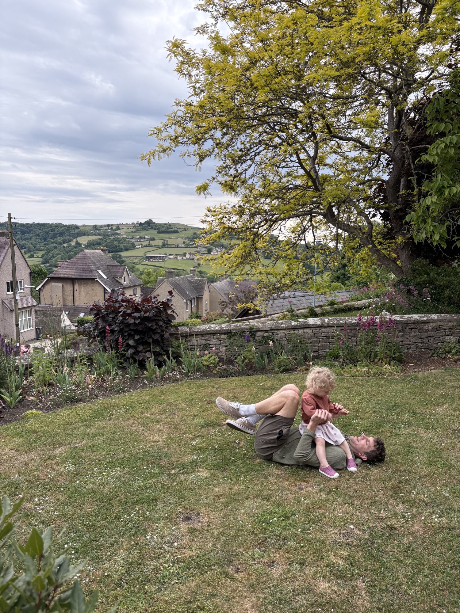 A garden overlooking rolling green hills and stone cottages in the English countryside.